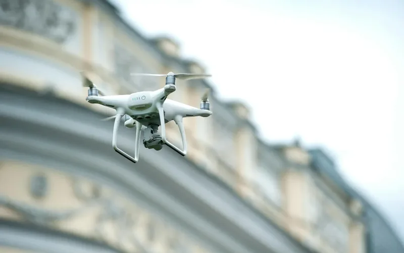 Drone branco de entrega sobrevoando área urbana com uma encomenda acoplada