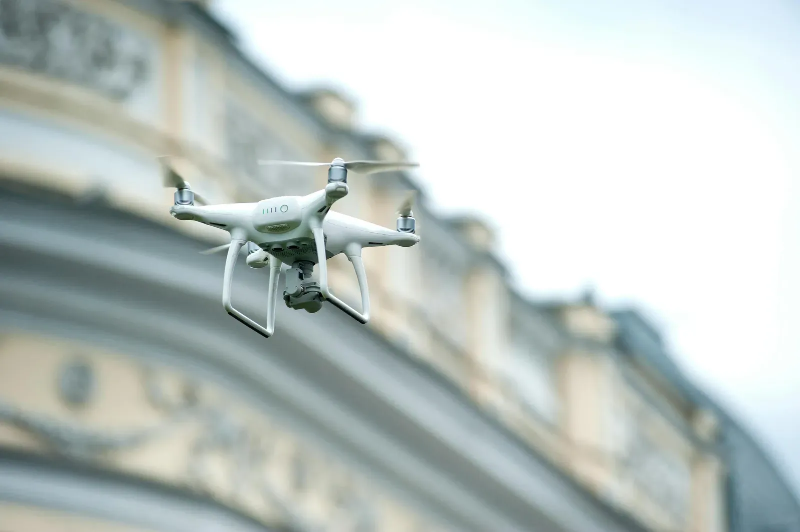 Drone branco de entrega sobrevoando área urbana com uma encomenda acoplada