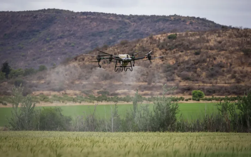 Agricultural spray drone releasing pesticide mist above a green crop field