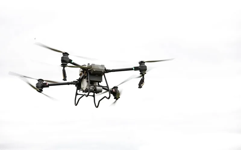 Commercial quadcopter drone flying above rural farmland under a clear sky