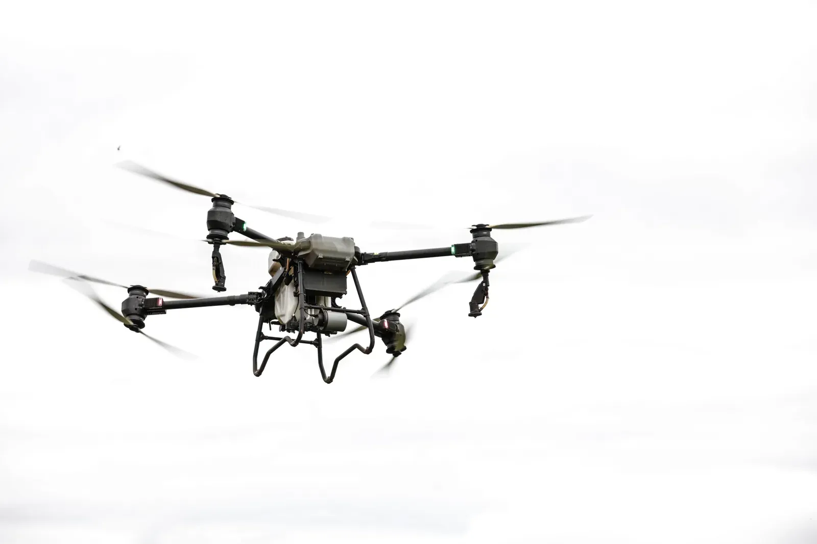 Commercial quadcopter drone flying above rural farmland under a clear sky