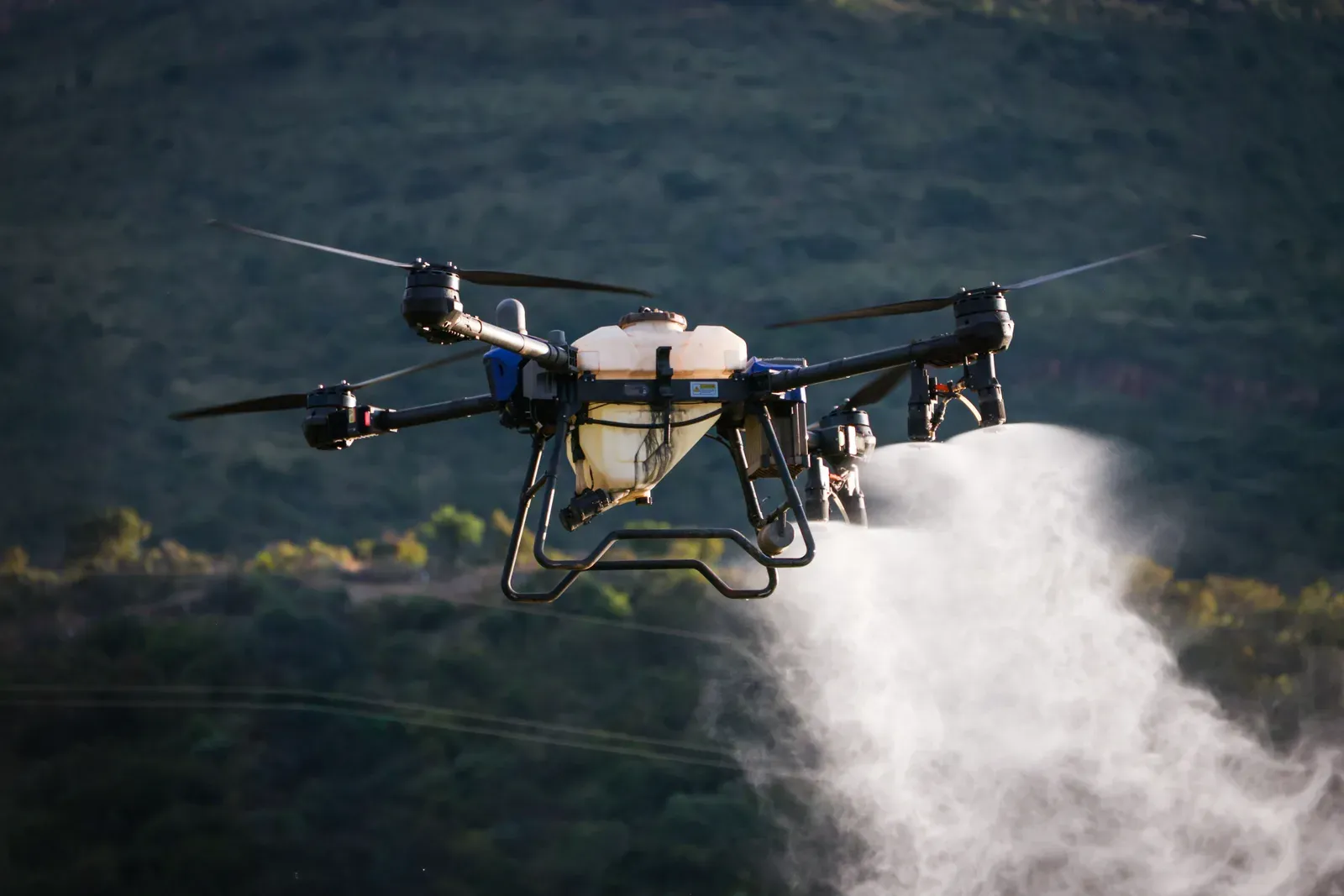 Heavy agricultural quadcopter spraying pesticide over rows of crops