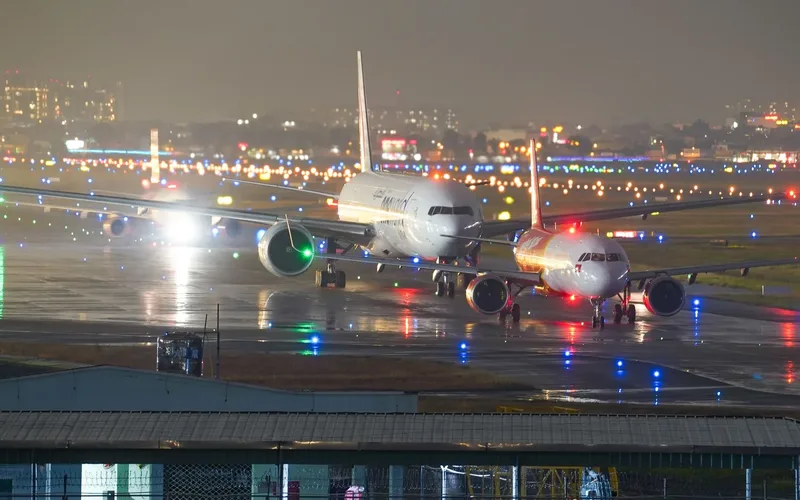 Torre de controle de aeroporto iluminada à noite com pista deserta ao fundo