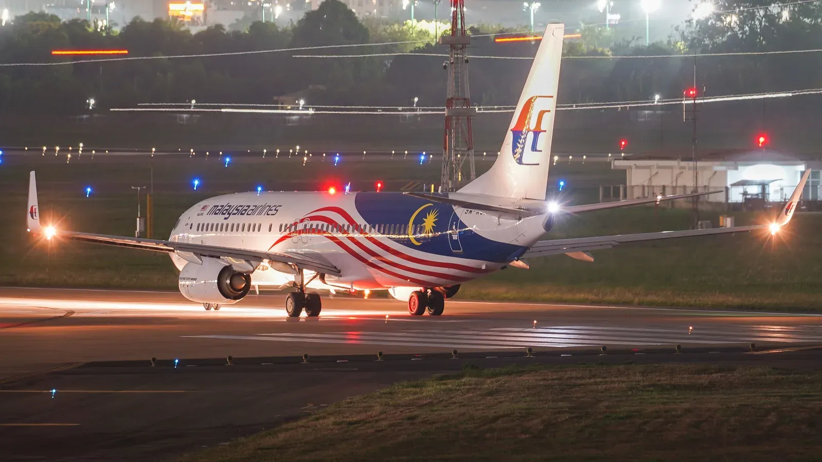 Torre de controle de aeroporto iluminada durante a noite com pista ao fundo